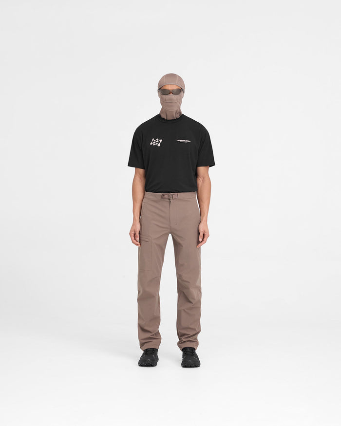 Man wearing nylon stretch pants in brown on a plain white background | 247 Mission Pant in Umber | Pants with zip pockets and built-in belt | 247 Pants | Represent Clo