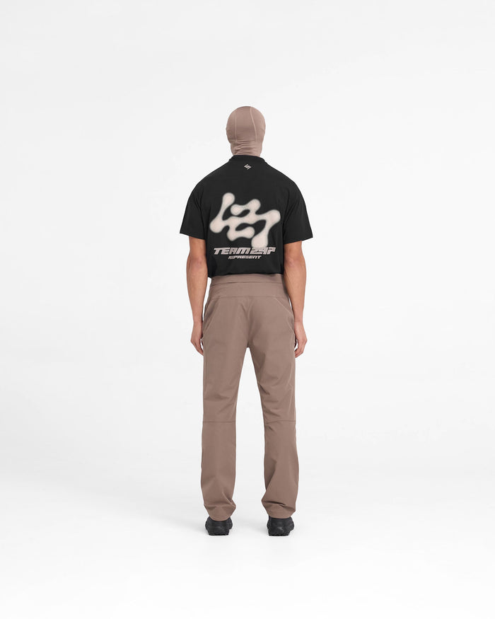 Man wearing umber pants on a plain white background | 247 Mission Pant in Umber | Pants with knee articulation and zip pockets | 247 Pants | Represent Clo