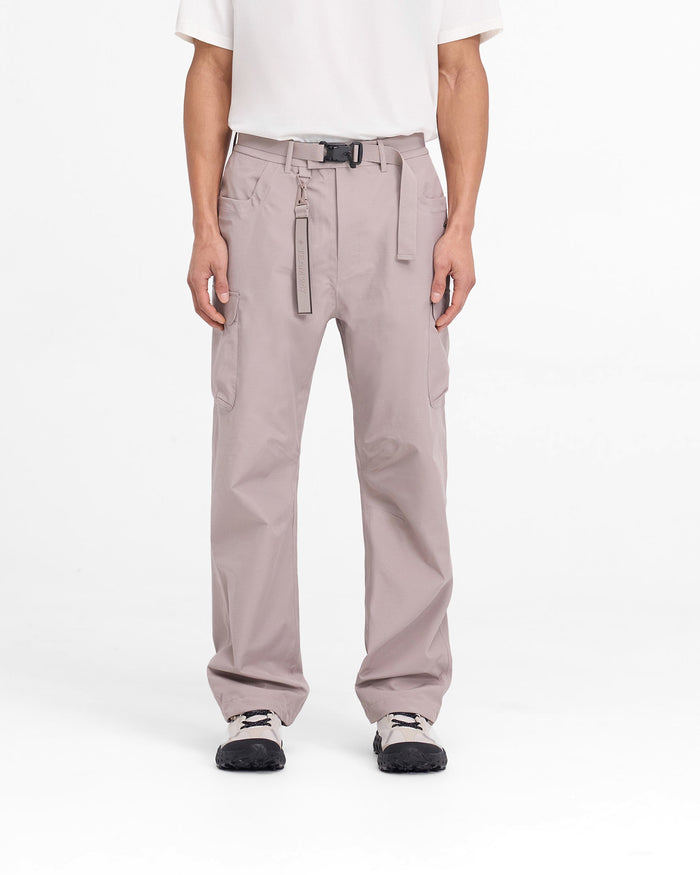 Man wearing grey technical cargo pants on a plain white background | 247 Technical Cargo Pant in Moonrock | Straight leg showerproof pants with maglock buckle and knee darts | 247 Pants | Represent Clo