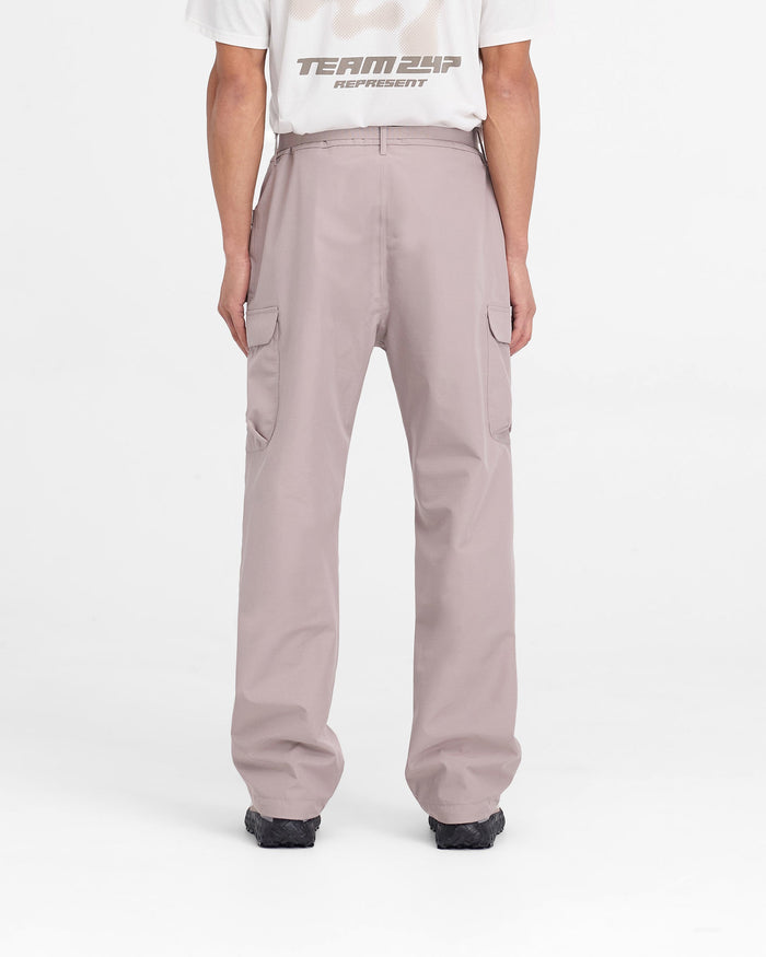 Man wearing grey technical cargo pants on a plain white background | 247 Technical Cargo Pant in Moonrock | Showerproof cargos with maglock buckle and bungee cord hem | 247 Pants | Represent Clo