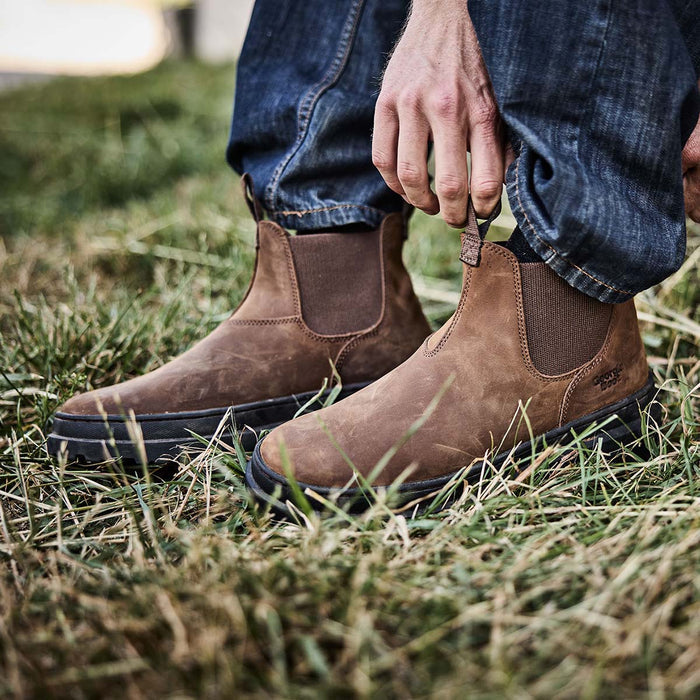 Brown boots worn with blue jeans on a grassy background